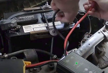 Closeup of mechanic's hands attaching wires to a car battery